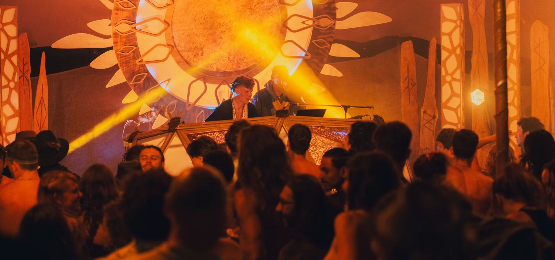 An ecstatic dance at night, glowing sun stage and a full dancefloor